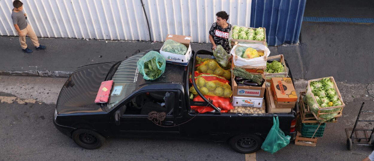 Black truck filled with various fresh vegetables parked on city street, viewed from above.